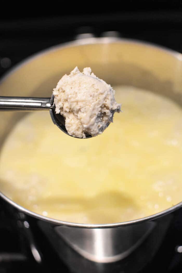 A spoonful of ricotta curds held over a pot of simmering liquid on a stove evokes the comforting warmth of classic Bisquick recipes like Chicken and Dumplings.