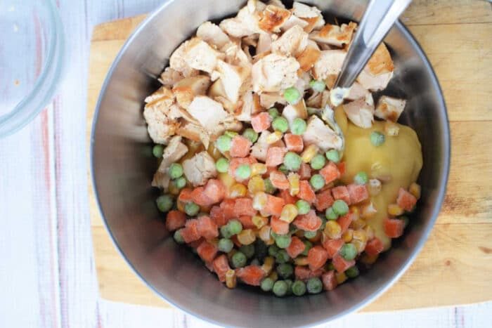 A metal bowl with chopped chicken, frozen mixed vegetables, creamy soup, and Bisquick on a wooden cutting board—solid for making Chicken and Dumplings.