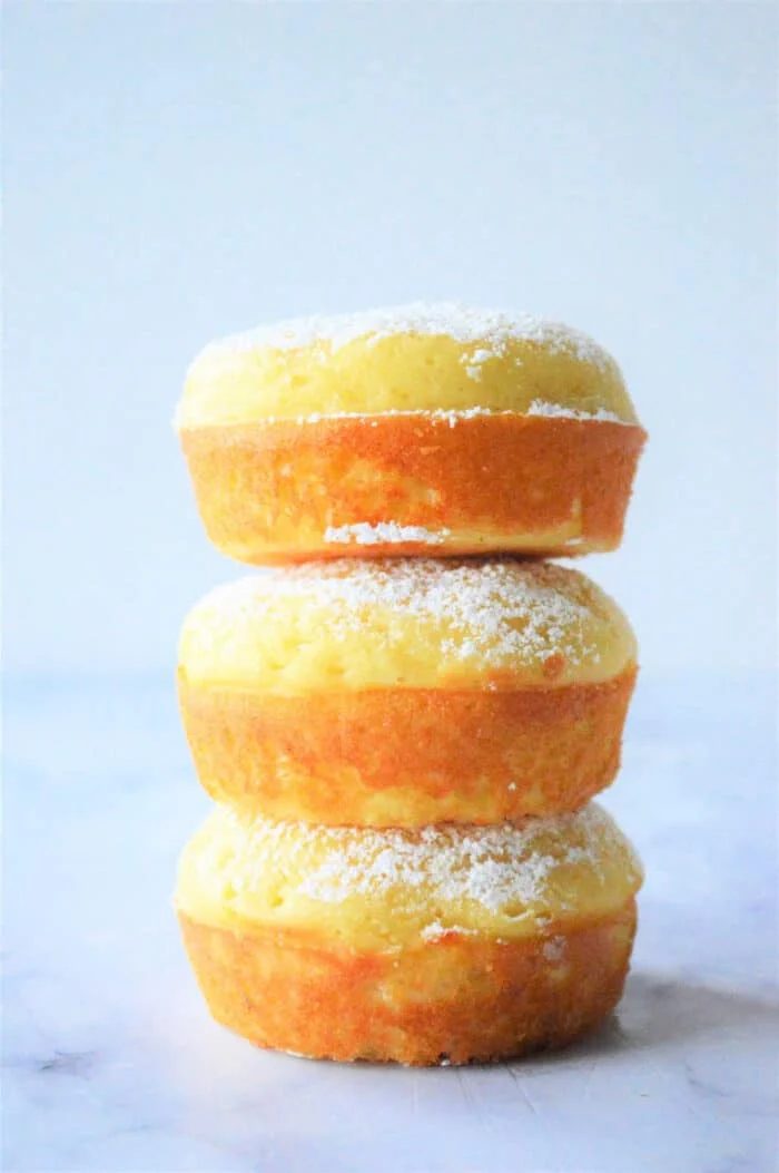Three stacked lemon fluffy Bisquick muffins, are delicately dusted with powdered sugar on a light background.