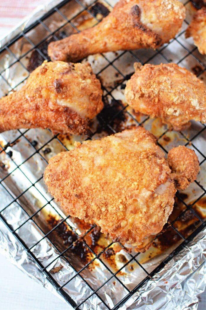 Golden, crispy oven fried chicken pieces rest on a wire rack over foil, showcasing their perfectly seasoned coating.