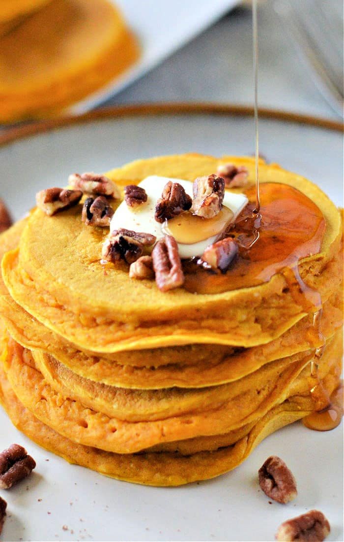 A stack of pumpkin pancakes made with Bisquick, topped with butter, pecans, and a drizzle of syrup.