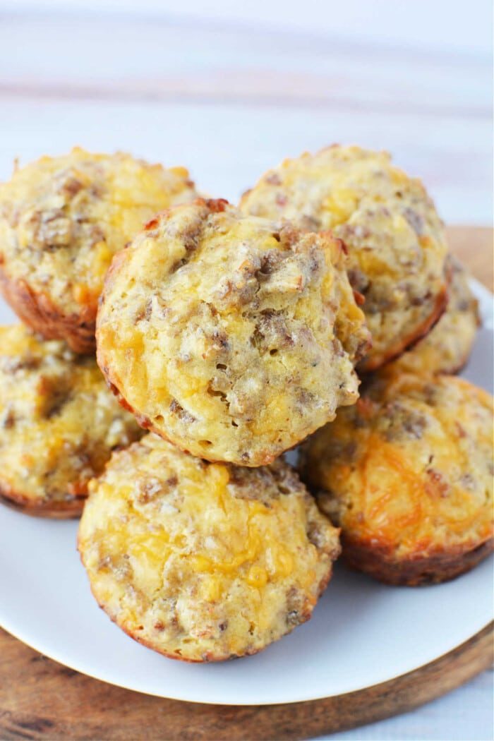 A plate of golden-brown sausage Bisquick muffins with visible chunks, arranged in a stack on a wooden surface.