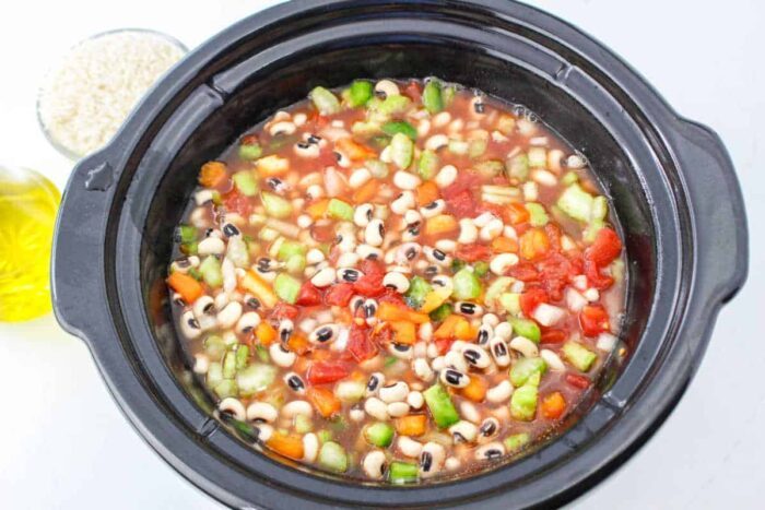 A slow cooker filled with black-eyed peas, diced tomatoes, carrots, celery, broth, and ready for cooking—add rice to create a comforting Black Eyed Peas and Rice dish.