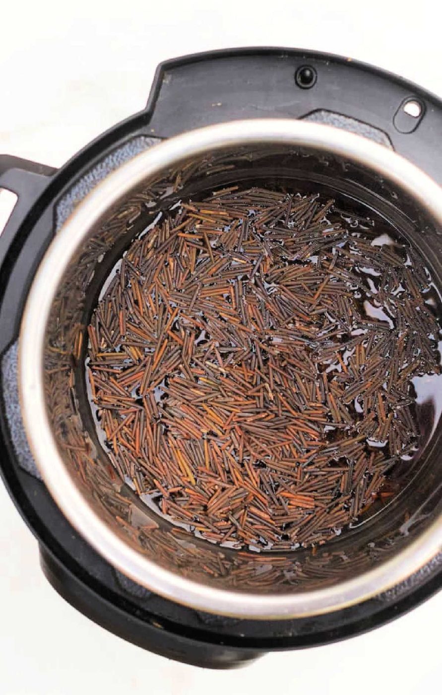 Uncooked wild and black rice soaking in water inside an Instant Pot, viewed from above.