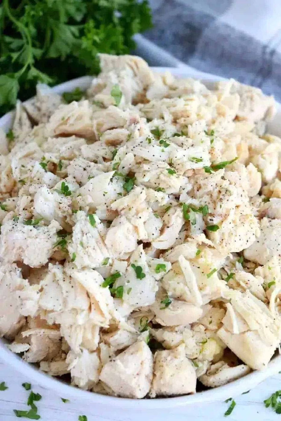 A bowl of shredded cooked chicken, garnished with chopped parsley and black pepper—solid for anyone learning how to make shredded chicken on the stove.