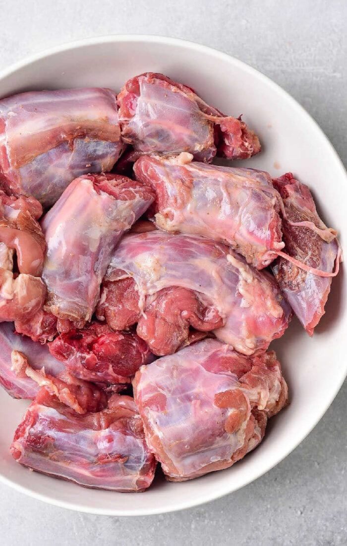 A white bowl filled with raw turkey neck pieces sits on a gray surface, reminiscent of preparing boiled turkey necks.
