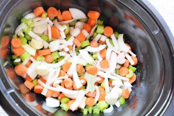 Chopped carrots, celery, onions, and potatoes simmer in a savory broth recipe within the slow cooker.