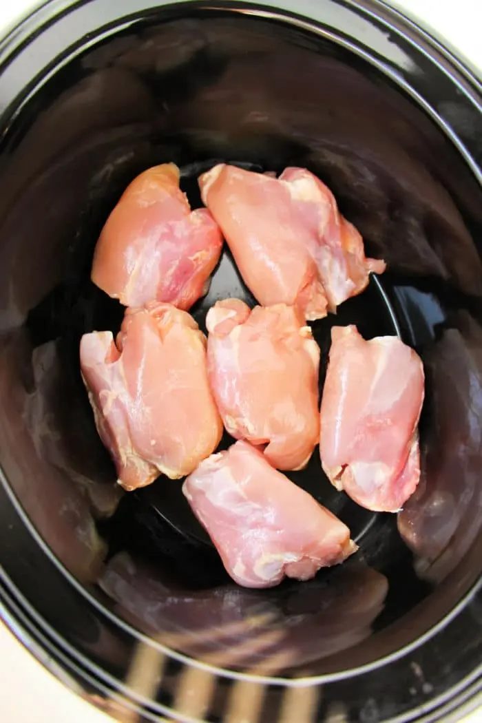Boneless, skinless chicken thighs nestled in a black crockpot await their transformation into a good meal.