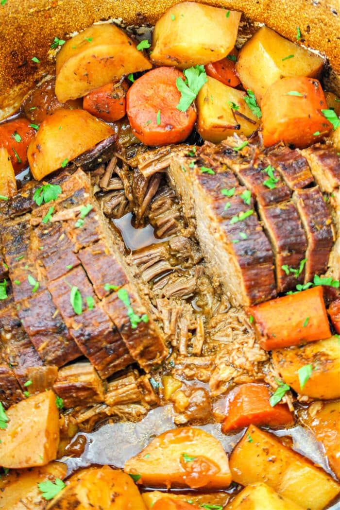 Sliced chuck roast with potatoes and carrots in a red wine seasoned broth, garnished with chopped parsley.