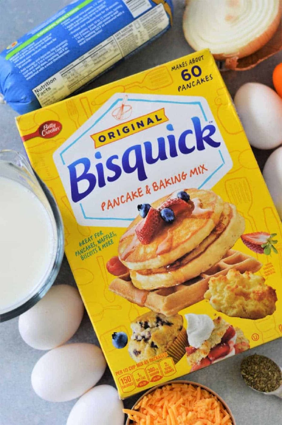 Box of Bisquick mix surrounded by eggs, milk, shredded cheese, an onion, and a roll of sausage—everything you need for a good Breakfast Casserole with Bisquick.