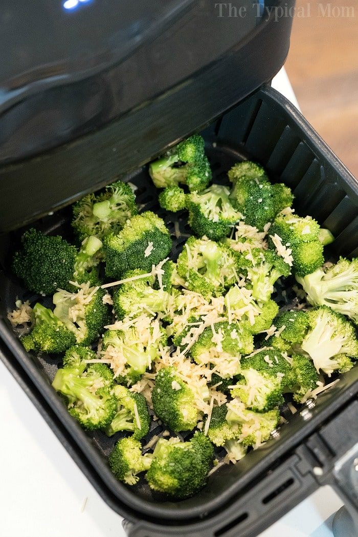Fresh broccoli florets with shredded cheese sit in an air fryer basket, solid for making good broccoli in air fryer.
