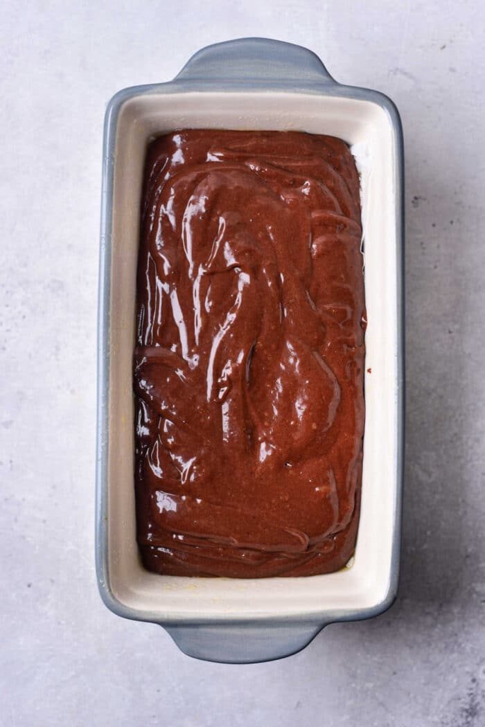 A rectangular baking dish filled with smooth, uncooked Brownie Bread batter rests on a light surface, promising a rich chocolate treat.
