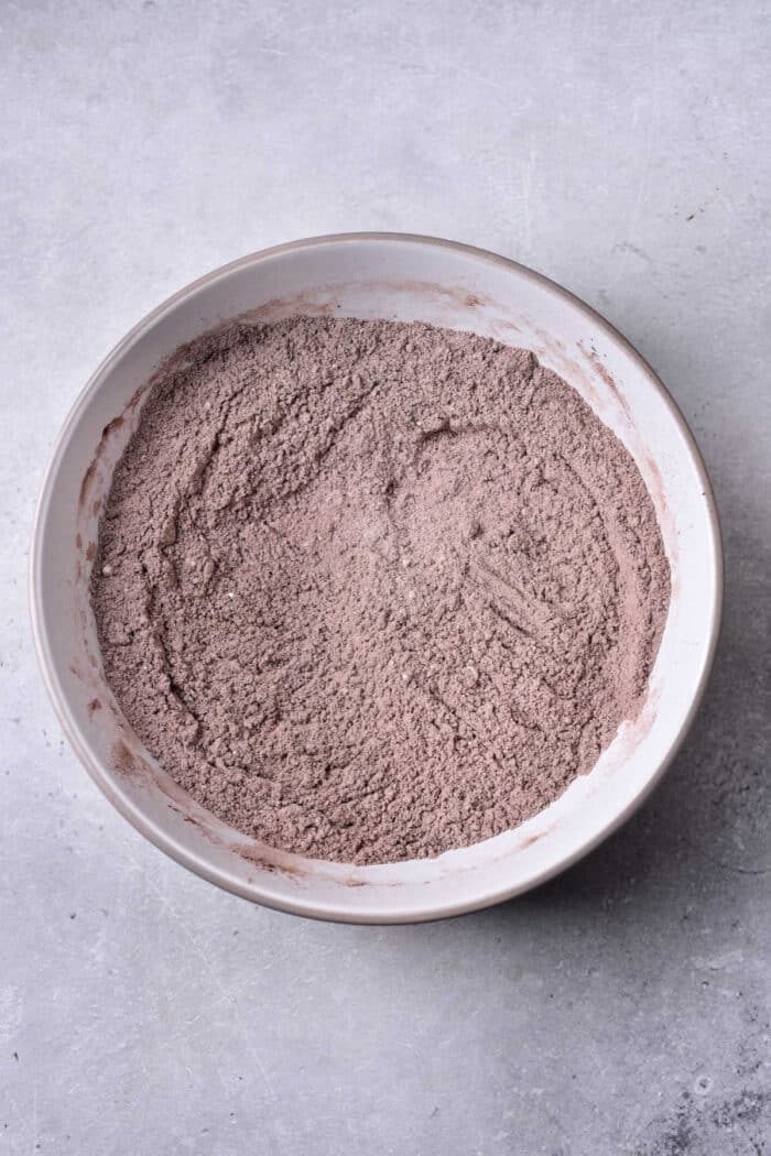 A bowl of mixed cocoa powder, solid for whipping up a delightful brownie bread, sits gracefully in a white bowl on a textured gray surface.