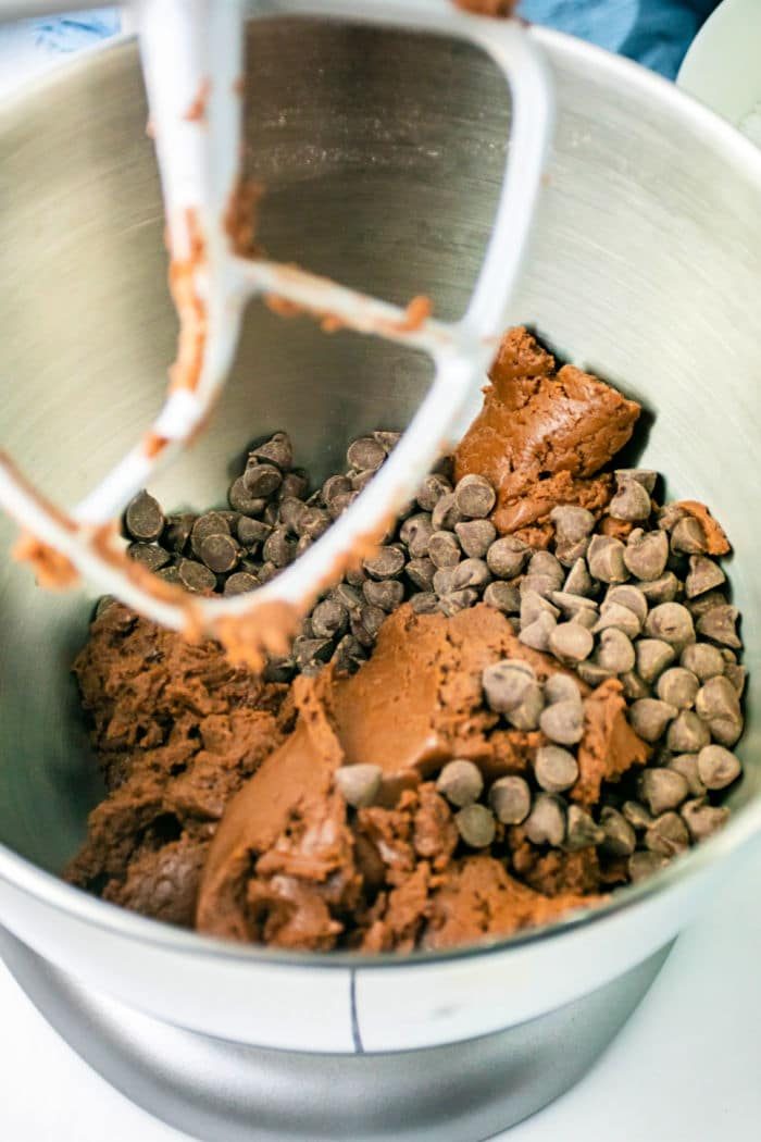 A mixing bowl with chocolate chip cookie dough and a paddle attachment. The dough is thick, reminiscent of brownie mix, with visible chocolate chips scattered throughout. The mixer waits eagerly to blend the ingredients into crinkle cookies perfection.