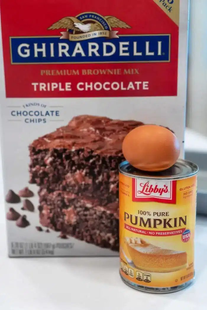 A box of Ghirardelli triple chocolate brownie mix is cleverly paired with a can of Libby's 100% pure pumpkin, hinting at the delightful creation of pumpkin brownies. An egg perches atop the can, ready to bring this good idea to life.