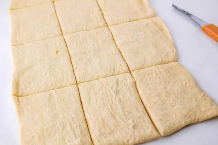 Sheets of crescent sheet are cut into neat rectangular pieces, with a knife resting nearby on a pristine white surface.