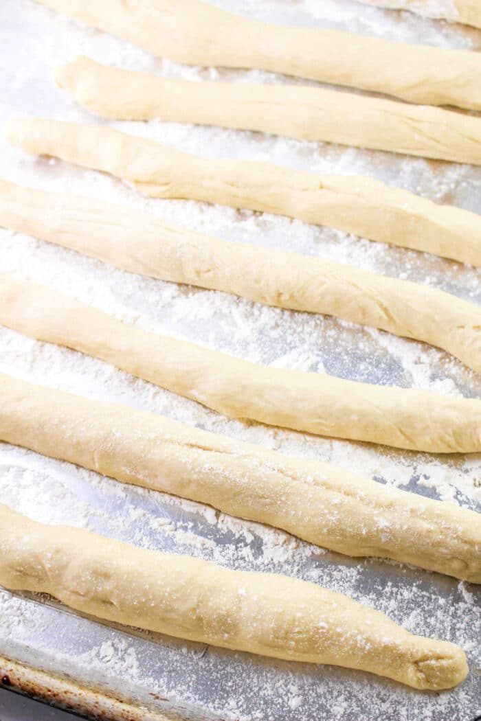 Raw breadsticks, reminiscent of a classic Bunny Bread recipe, are arranged on a floured baking sheet.