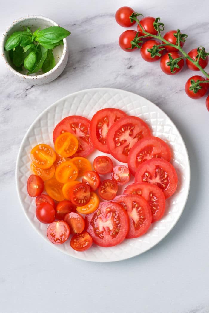 A plate of sliced red and yellow tomatoes accompanied by creamy burrata, with a sprig of fresh basil nearby, creates a delightful Caprese experience.