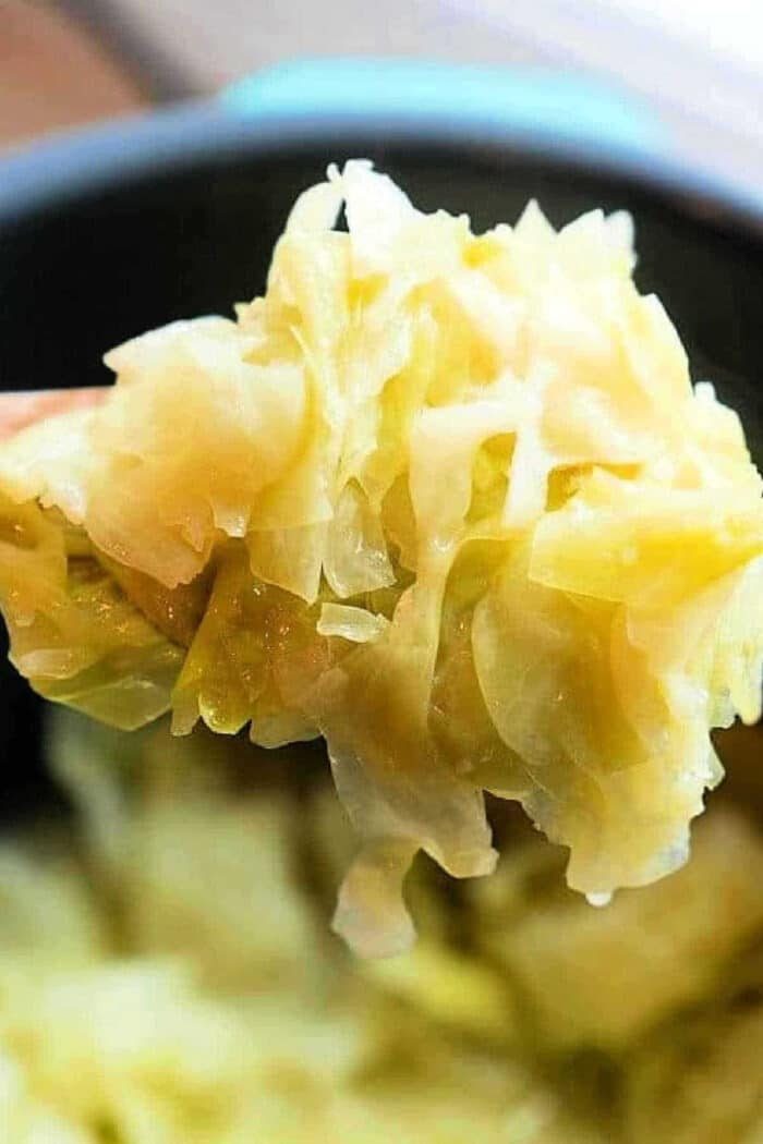 A spoonful of cooked, shredded cabbage is held up close above a pot of more tender Buttered Pressure Cooker Cabbage.