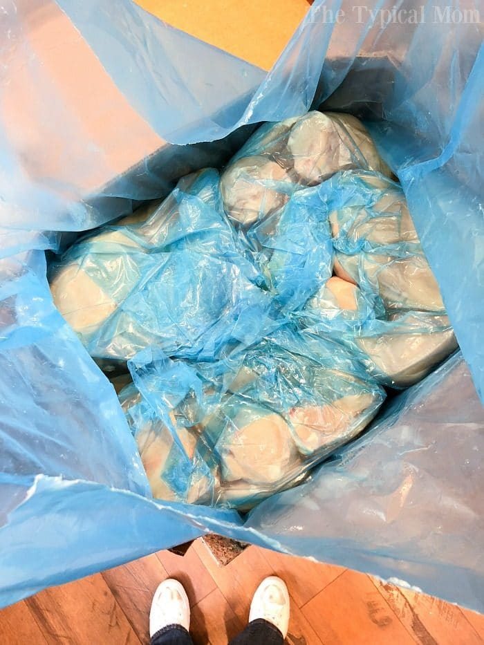 A cardboard box filled with chicken wrapped in blue plastic bags, solid for anyone buying chicken in bulk, rests on a wooden floor.