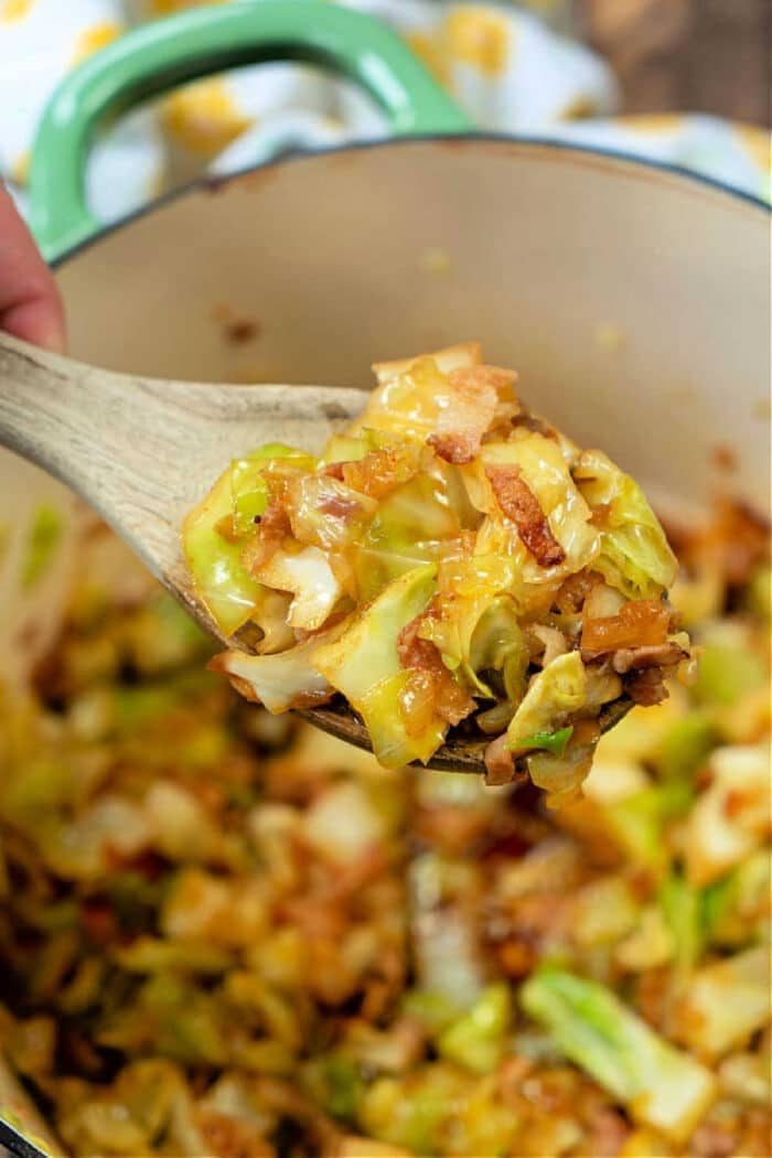 A wooden spoon lifts a good mixture, embodying the solid cabbage and bacon recipe, right from the pot.