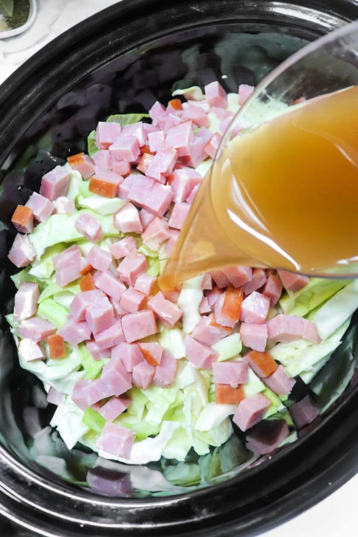 Simmering a delightful mix of cabbage and ham, pour broth over the diced ingredients in a slow cooker for a comforting meal.