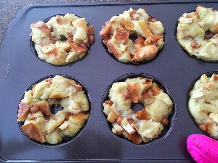 A baking tray with six muffin-shaped bread puddings, filled with chunks of bread and bits of fruit or nuts, transforms into caramel apple bread puddings with a luscious drizzle that adds a sweet finish.