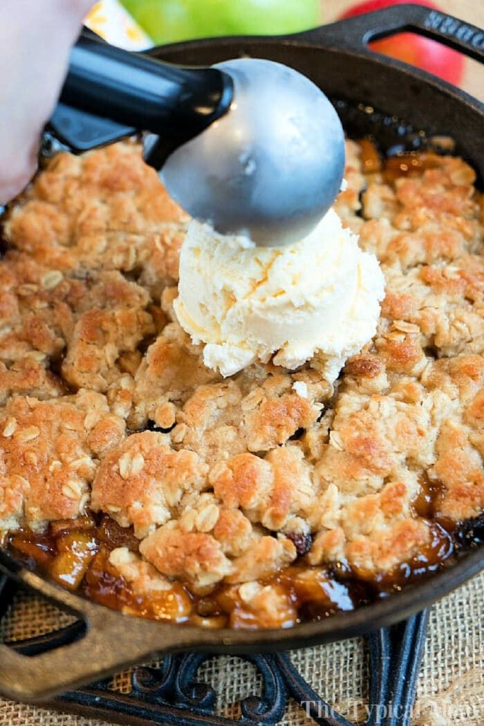 Scooping vanilla ice cream onto a freshly baked apple crisp in a cast iron skillet brings the delightful aroma of warm spices and fruit, much like a classic cast iron apple crisp.