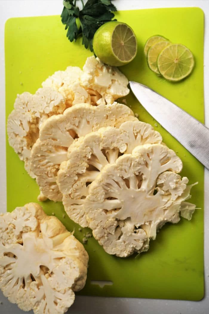 Sliced cauliflower, lime, and a knife on a green cutting board with parsley in the background—solid ingredients for making cauliflower steak in the air fryer.