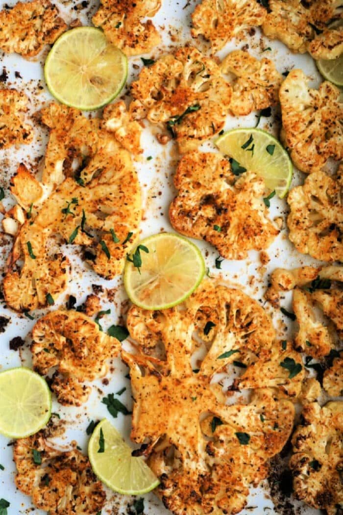 Roasted cauliflower steak slices, expertly spiced and air-fried to perfection, are garnished with lime and herbs on a pristine white surface.