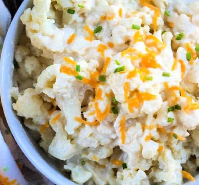 A bowl of cheesy cauliflower, effortlessly creamy from the Instant Pot, is topped with shredded cheese and a sprinkle of chopped chives.