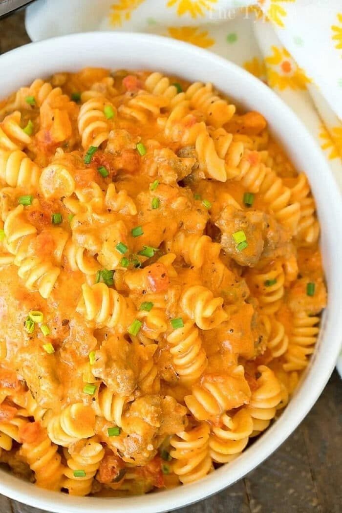 A bowl of creamy rotini pasta with ground meat, diced tomatoes, and chopped chives on top—this dish brings the comfort of cheesy Instant Pot goulash to your table.