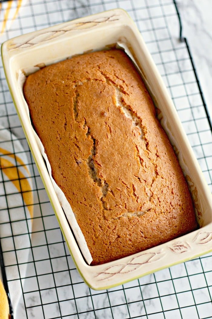 A freshly baked loaf of Cherry Bread in a rectangular ceramic pan rests on a cooling rack, its sweet aroma filling the air.