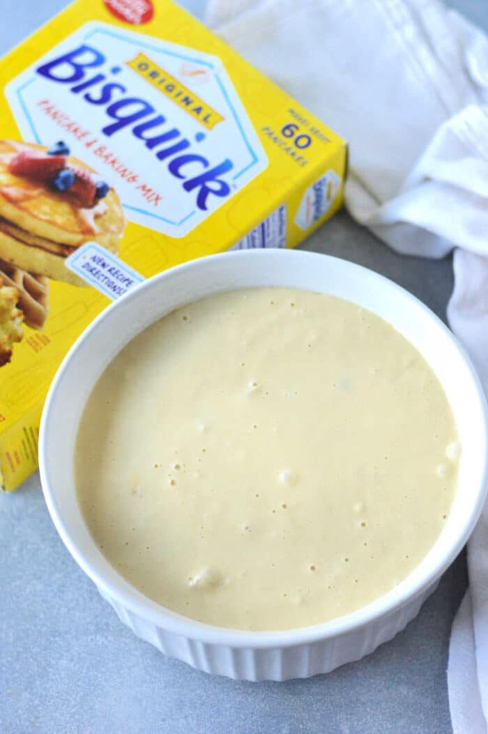 A bowl of bisquick batter sits invitingly next to a box of Bisquick pancake and baking mix on the countertop, perfectly ready to transform into the ultimate Chicken Cobbler Recipe delight.