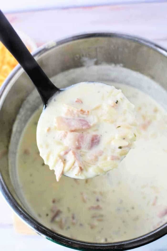 A ladle holding creamy ham and potato soup above a pot filled with the same comforting blend, reminiscent of hearty Chicken Crack Soup.