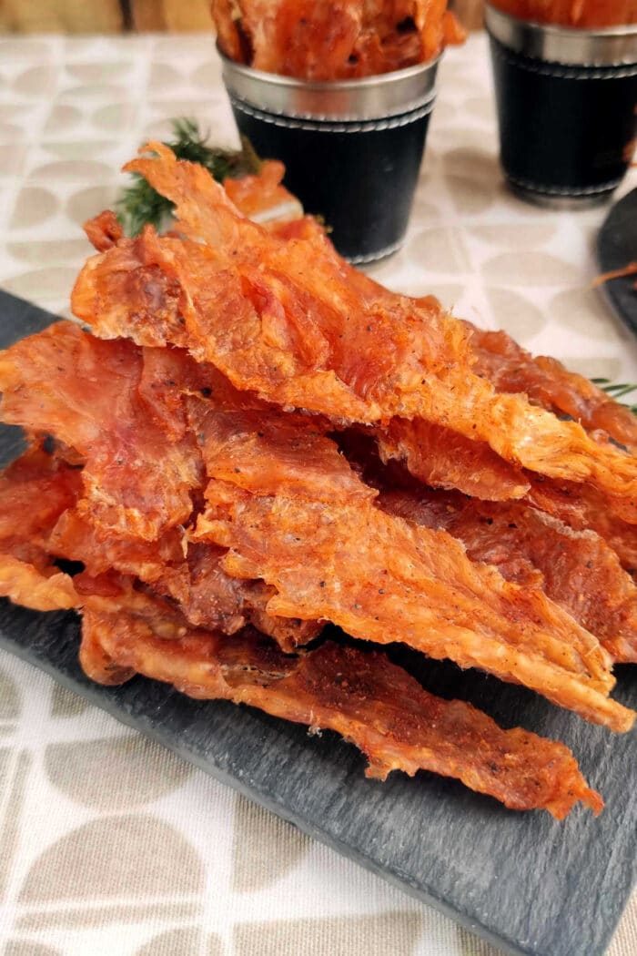 A stack of crispy chicken jerky on a slate serving board.