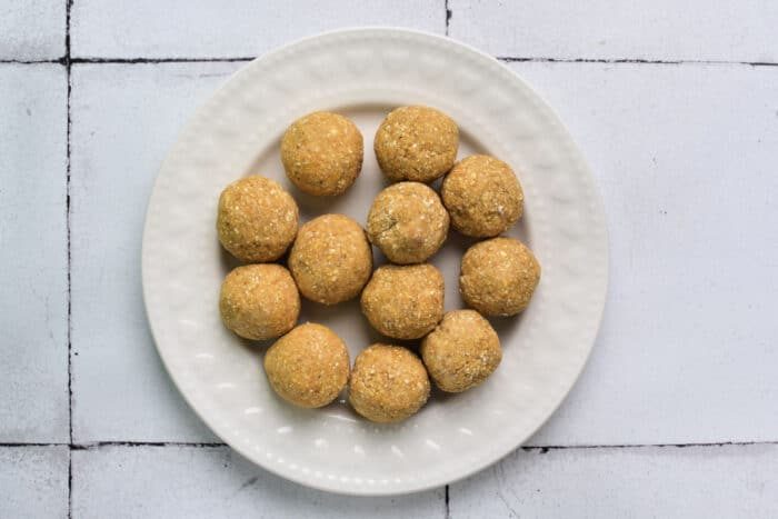 A plate of round, golden-brown matzo balls is artfully arranged on a white, textured background, reminiscent of warm, comforting moments shared over bowls of chicken matzo ball soup.