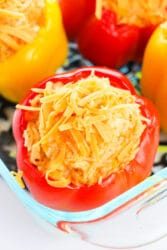 Chicken stuffed red and yellow bell peppers filled with cheese and rice, all nestled in a glass dish.