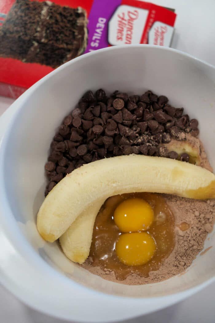 A mixing bowl with eggs, banana, chocolate chips, and cake mix—solid for whipping up easy chocolate banana bread; a cake mix box sits in the background.
