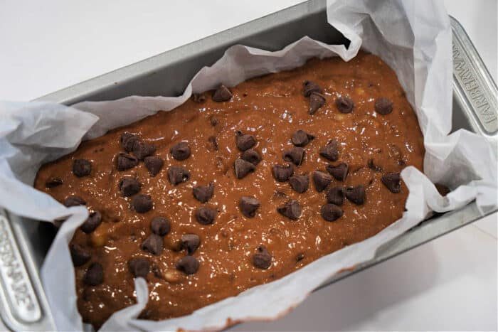 Chocolate Banana Bread batter with chocolate chips in a parchment-lined loaf pan, ready to be baked.