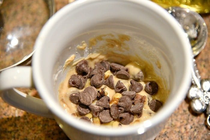 A delightful chocolate chip cookie in a mug brimming with gooey dough and rich chocolate chips sits invitingly on the kitchen counter.