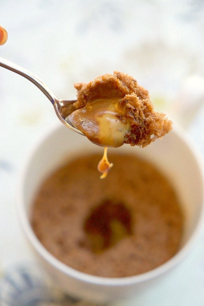 A spoon lifts a bite of molten caramel and chocolate mug cake with a gooey center above a white mug, tempting any dessert lover.