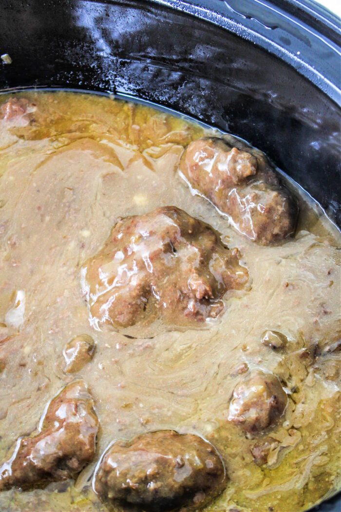 Beef tips covered in brown gravy simmer in a black slow cooker, creating a comforting Chopped Steak Recipe that's solid for any meal.