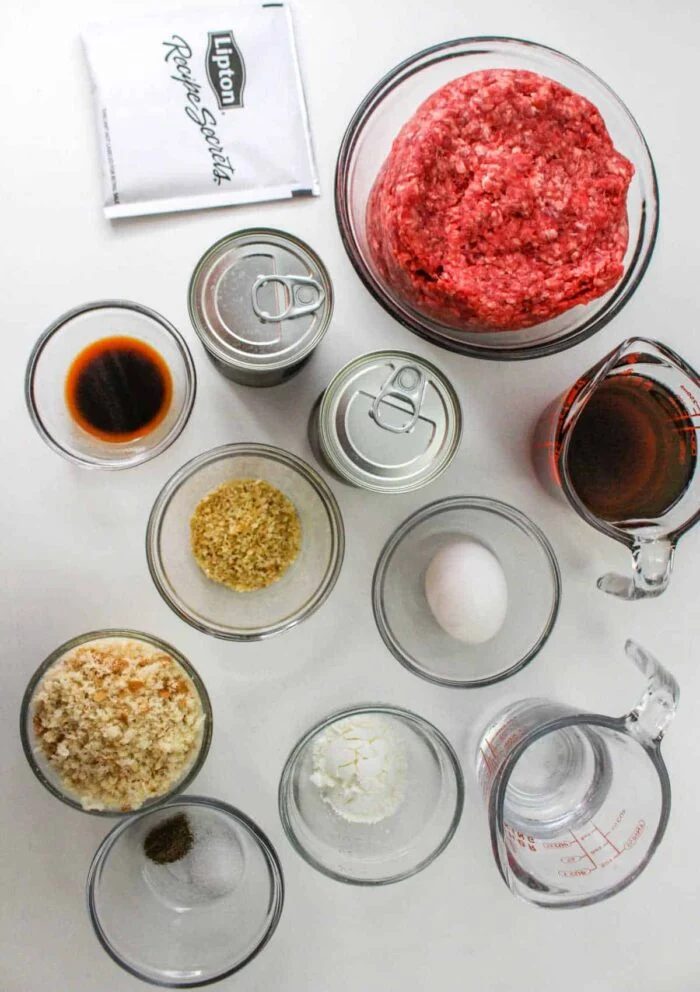 Top view of raw ground beef, seasonings, sauces, egg, breadcrumbs, and canned soup ingredients on a white surface—solid for making a classic Chopped Steak Recipe.