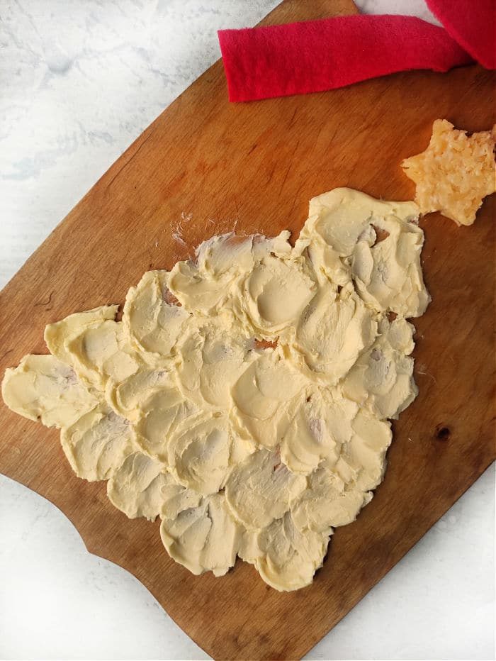 A festive Christmas tree-shaped butter spread adorns a wooden board, complete with a cheese star perched on top. solid for any holiday gathering, this creation elevates the traditional concept of a Christmas butter board into something truly special and delightful.
