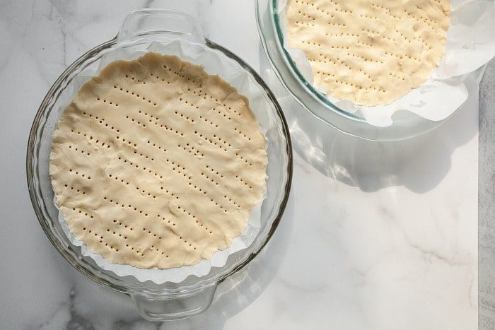 Two pie dishes on a marble surface, with fork marks on the cookie dough, evoke the charm of baking Christmas tree sugar cookies during the festive season.