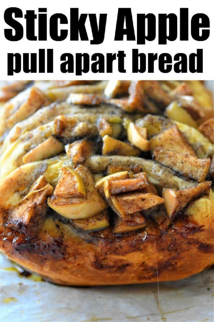 A loaf of sticky cinnamon pull apart bread is topped with baked apples and cinnamon, served warm on parchment paper.