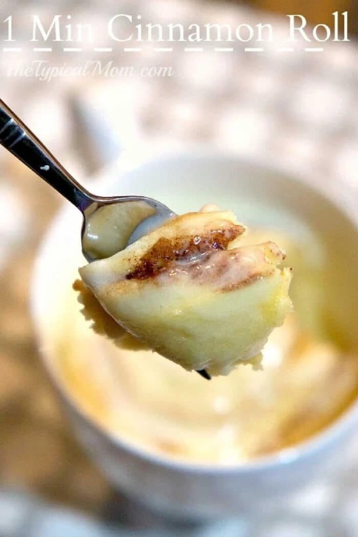 A fork holds a bite of cinnamon roll above a mug, with icing visible on the roll—solid for enjoying a warm cinnamon roll in a mug.