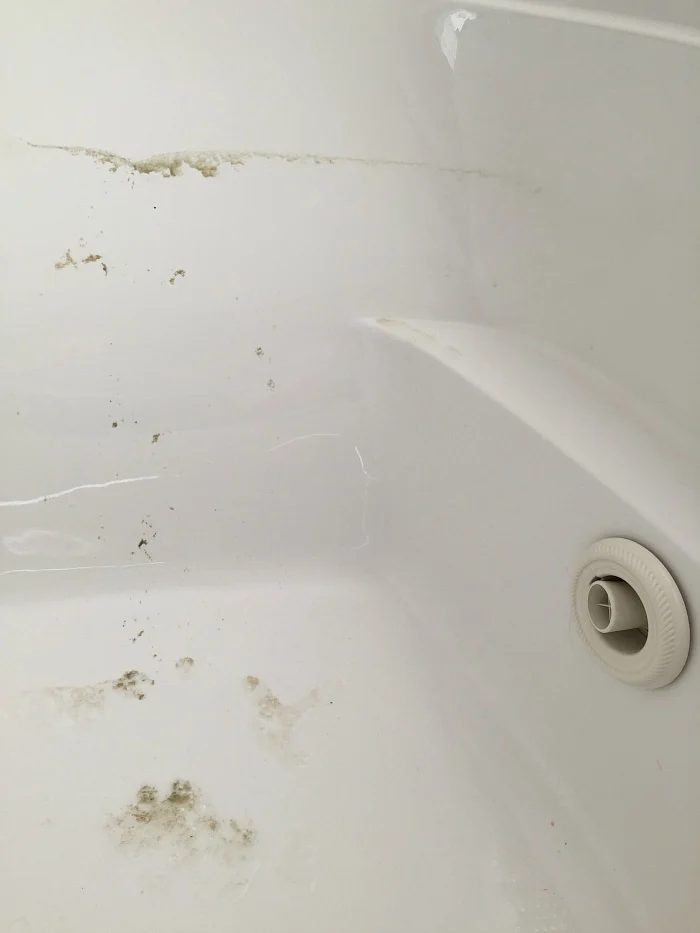 A close-up image of a white bathtub with noticeable mold and grime buildup around the edges and surface. The bathtub drain is partially visible in the bottom right corner. This jetted tub has visible dirt and requires thorough cleaning.