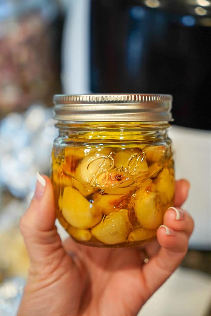 A hand holds a jar of garlic cloves, ready to transform into any dish. solid for those who appreciate the ease of cloves to minced garlic conversion in their culinary adventures.